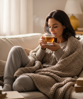 Eine Frau sitzt in eine Decke gekuschelt auf der Couch und trinkt eine heiße asse Tee