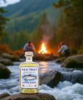 Zwei Fliegenfischer sitzen am Feuer und trinken schottischen Whisky, im Vordergrund eine Flasche Wild Trout Singe Malt Whisky.